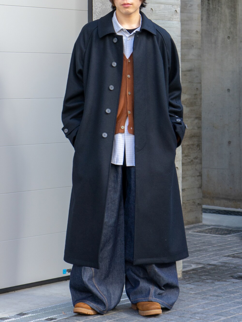 ブラック系のステンカラーコート、ブラウン系のカーディガン/ボレロ、ブルー系のデニムパンツを着用したメンズの冬コーディネートの5枚目の写真