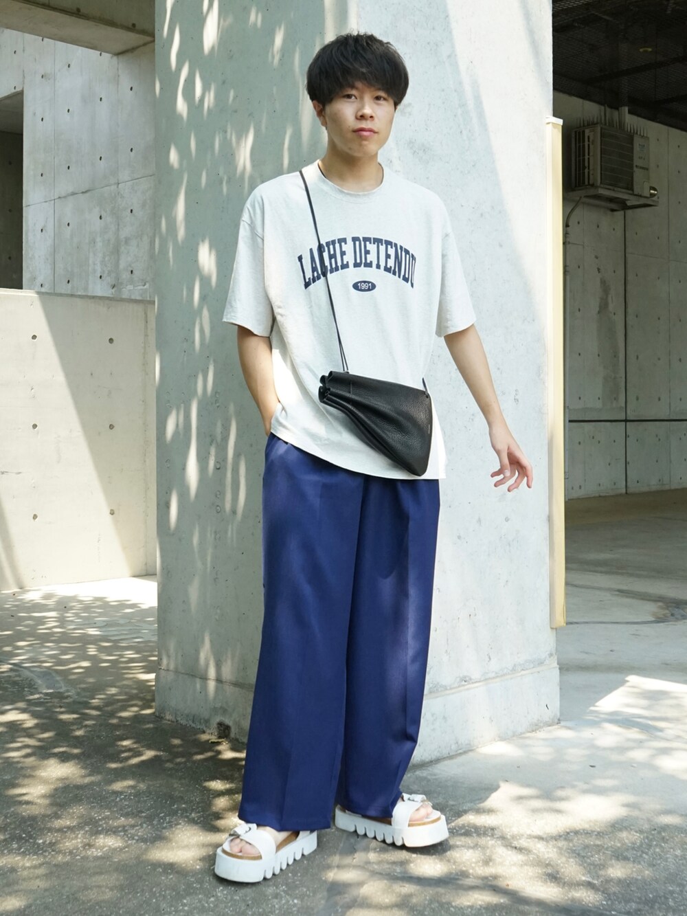 グレー系のTシャツ/カットソー、ブルー系のスラックス、ブラック系のショルダーバッグを着用したメンズの夏コーディネートの2枚目の写真