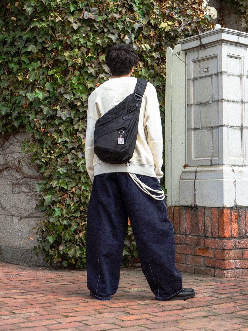 ホワイト系のスウェット、ブルー系のデニムパンツ、ブラック系のショルダーバッグを着用したメンズの春コーディネートの2枚目の写真