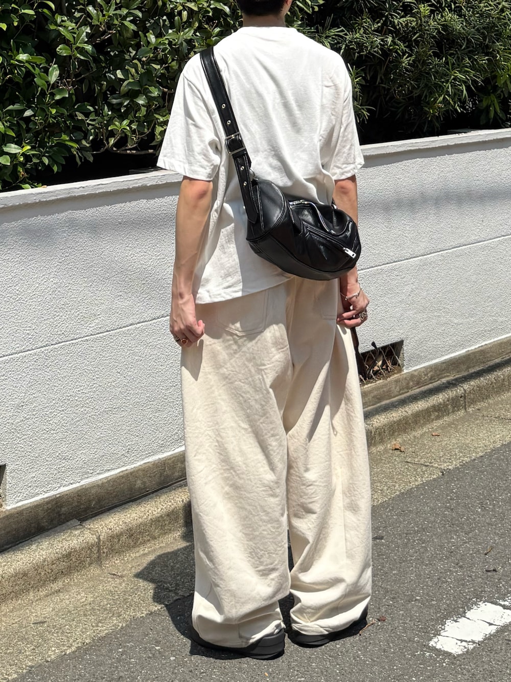 ホワイト系のTシャツ/カットソー、ブラック系のショルダーバッグ、ホワイト系のデニムパンツを着用したメンズの夏コーディネートの3枚目の写真