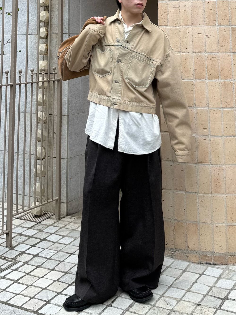 ベージュ系のデニムジャケット、ブラウン系のスラックス、ベージュ系のバッグを着用したメンズの春コーディネートの2枚目の写真