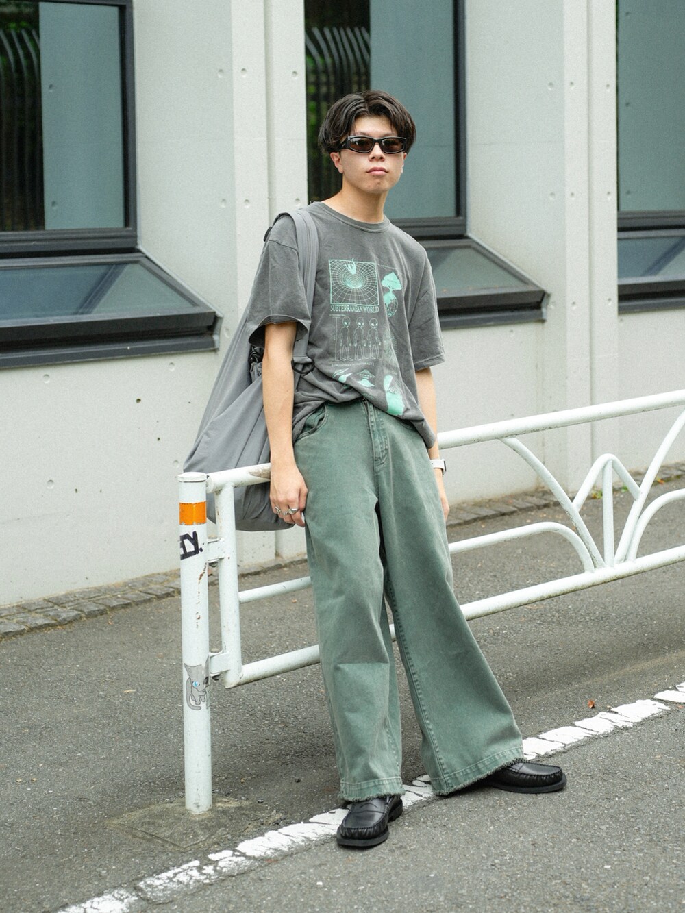 グレー系のショルダーバッグ、グリーン系のデニムパンツ、ブラック系のローファーを着用したメンズの夏コーディネートの2枚目の写真