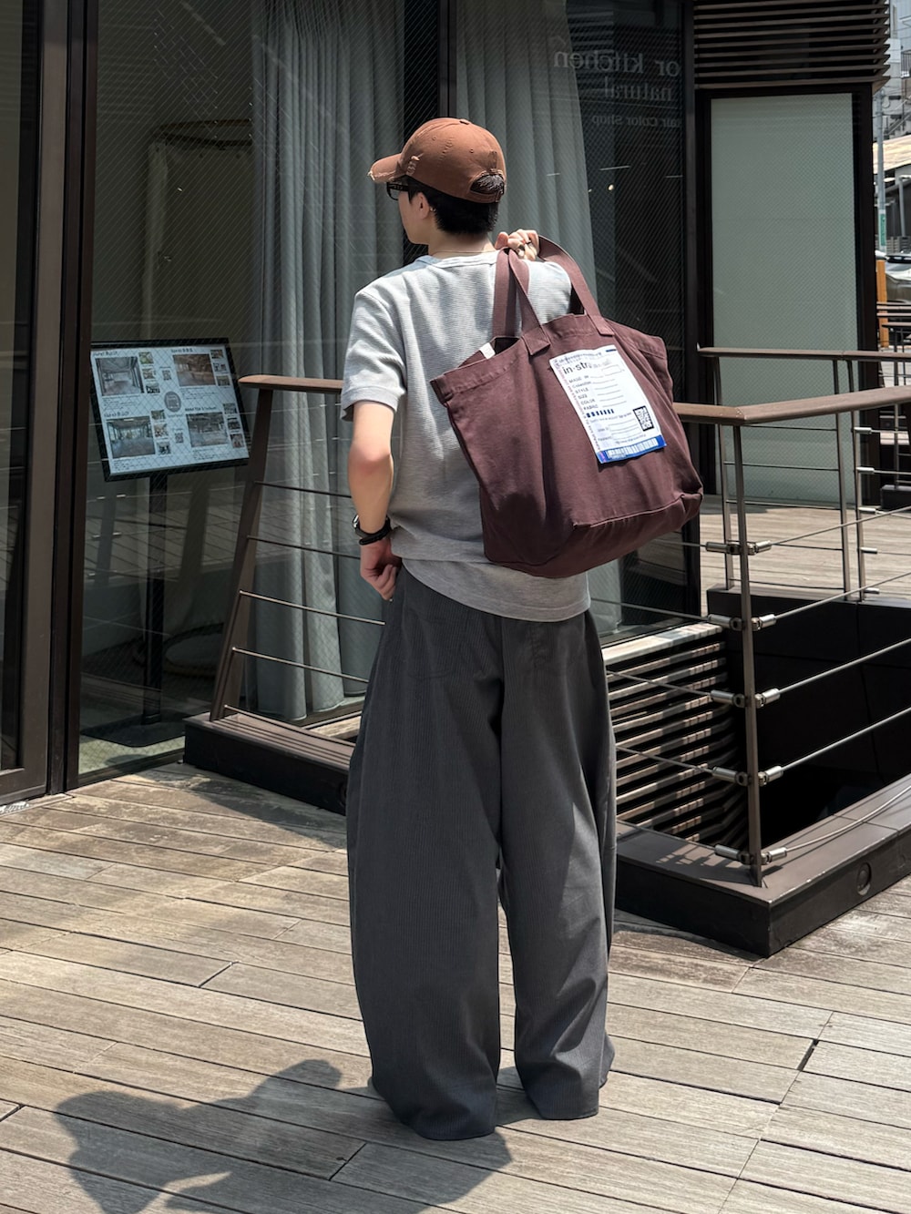 グレー系のTシャツ/カットソー、グレー系のスラックス、ブラウン系のトートバッグを着用したメンズの夏コーディネートの2枚目の写真