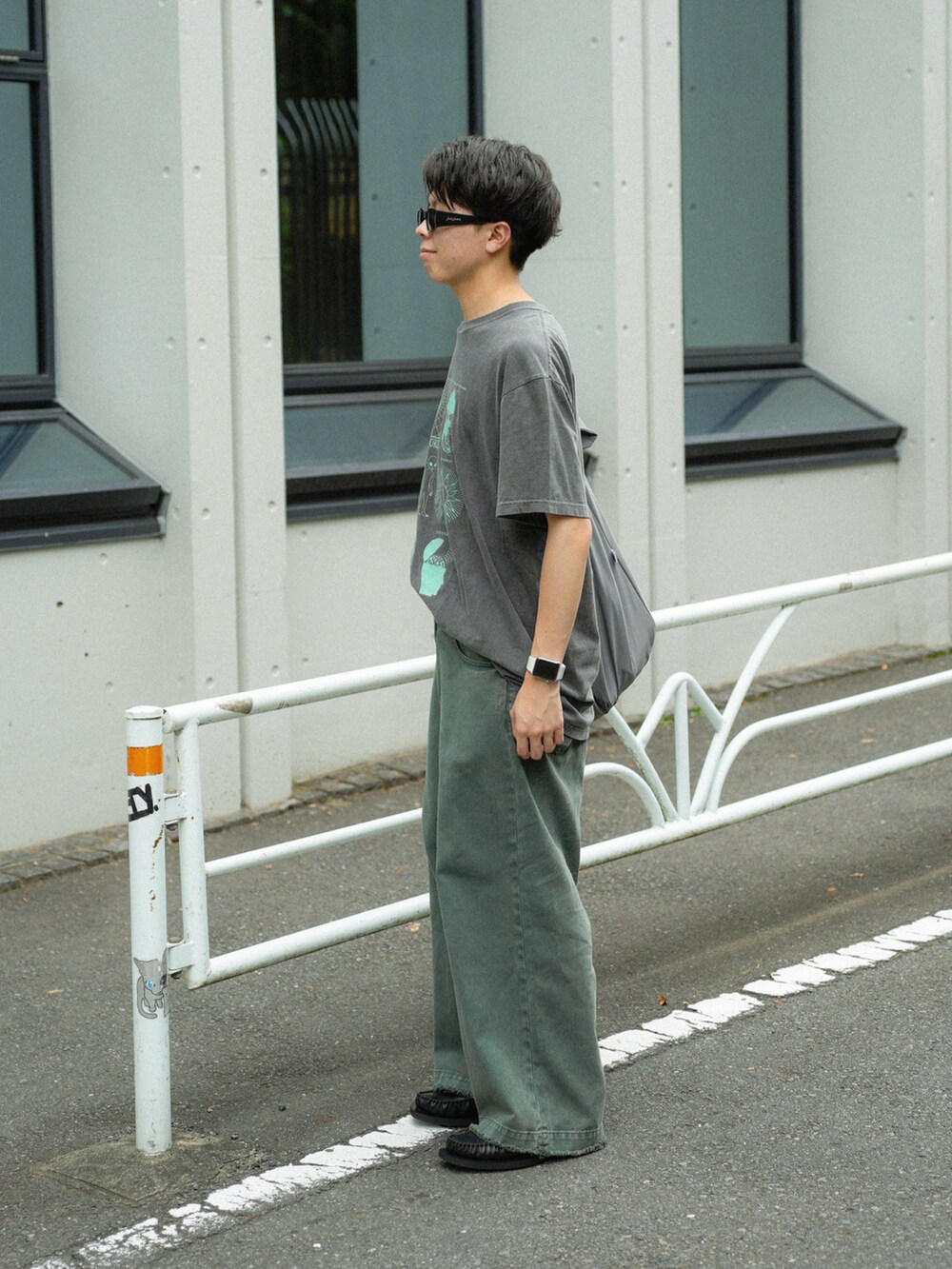 グレー系のショルダーバッグ、グリーン系のデニムパンツ、ブラック系のローファーを着用したメンズの夏コーディネートの3枚目の写真