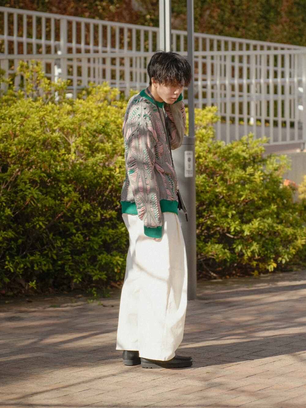 グリーン系のニット/セーター、ホワイト系のチノパンツ、ブラック系のショルダーバッグを着用したメンズの冬コーディネートの2枚目の写真