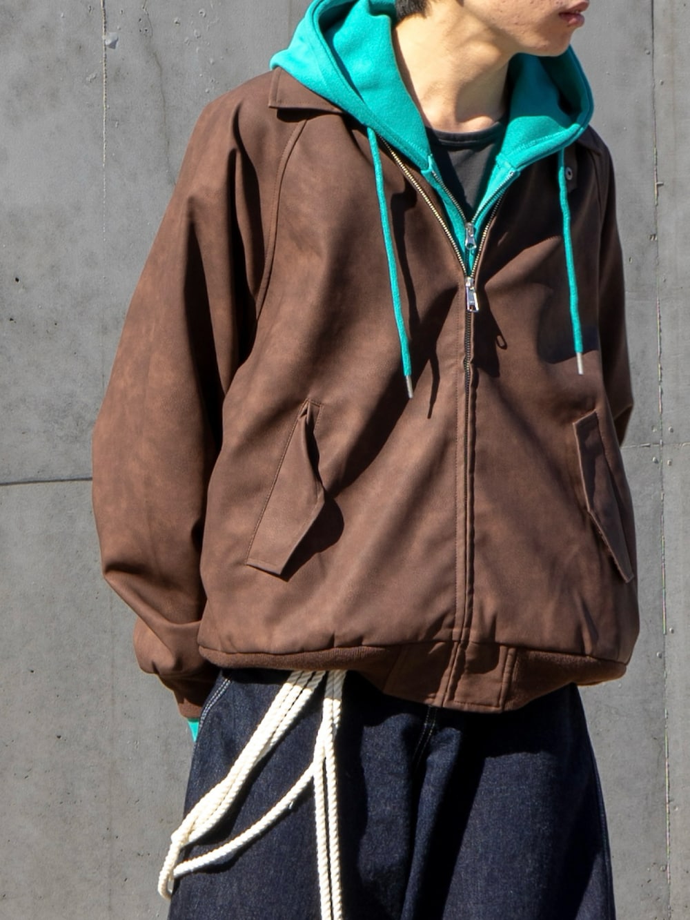 ブラウン系のブルゾン、ブルー系のパーカー、ブルー系のデニムパンツを着用したメンズの秋コーディネートの4枚目の写真