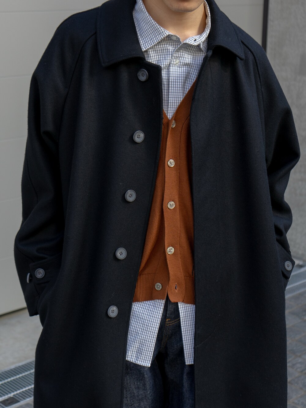 ブラック系のステンカラーコート、ブラウン系のカーディガン/ボレロ、ブルー系のデニムパンツを着用したメンズの冬コーディネートの4枚目の写真