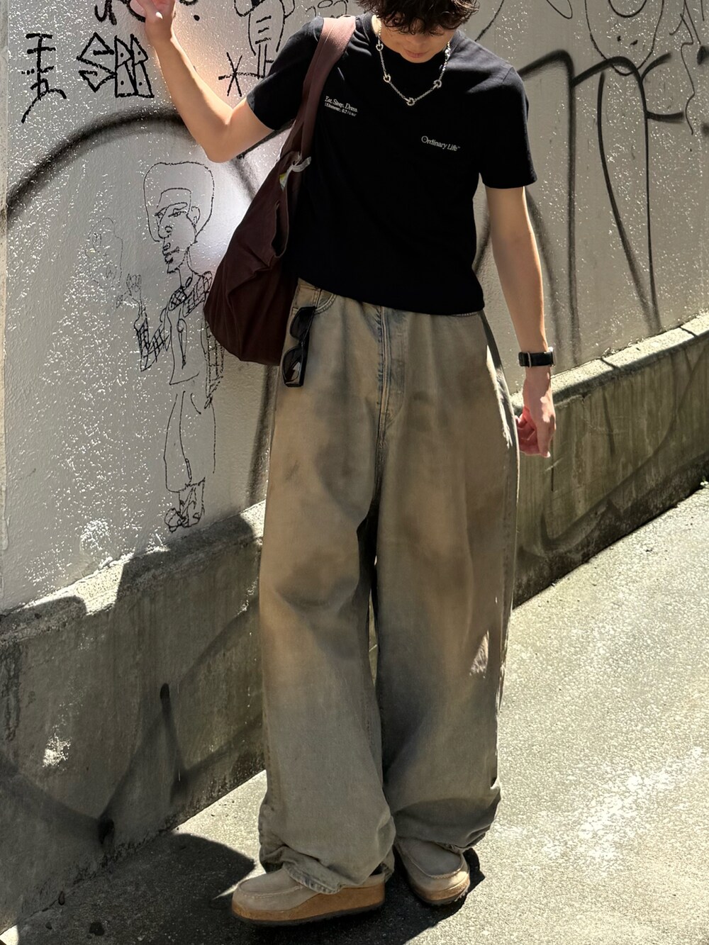 ブラック系のTシャツ/カットソー、ブルー系のデニムパンツ、ブラウン系のトートバッグを着用したメンズの夏コーディネートの3枚目の写真