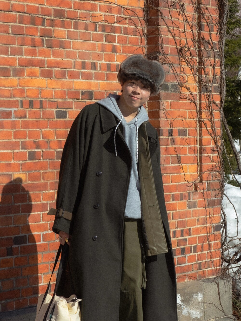 グリーン系のステンカラーコート、グレー系のパーカー、ブラック系のカバーオールを着用したメンズの春コーディネートの4枚目の写真