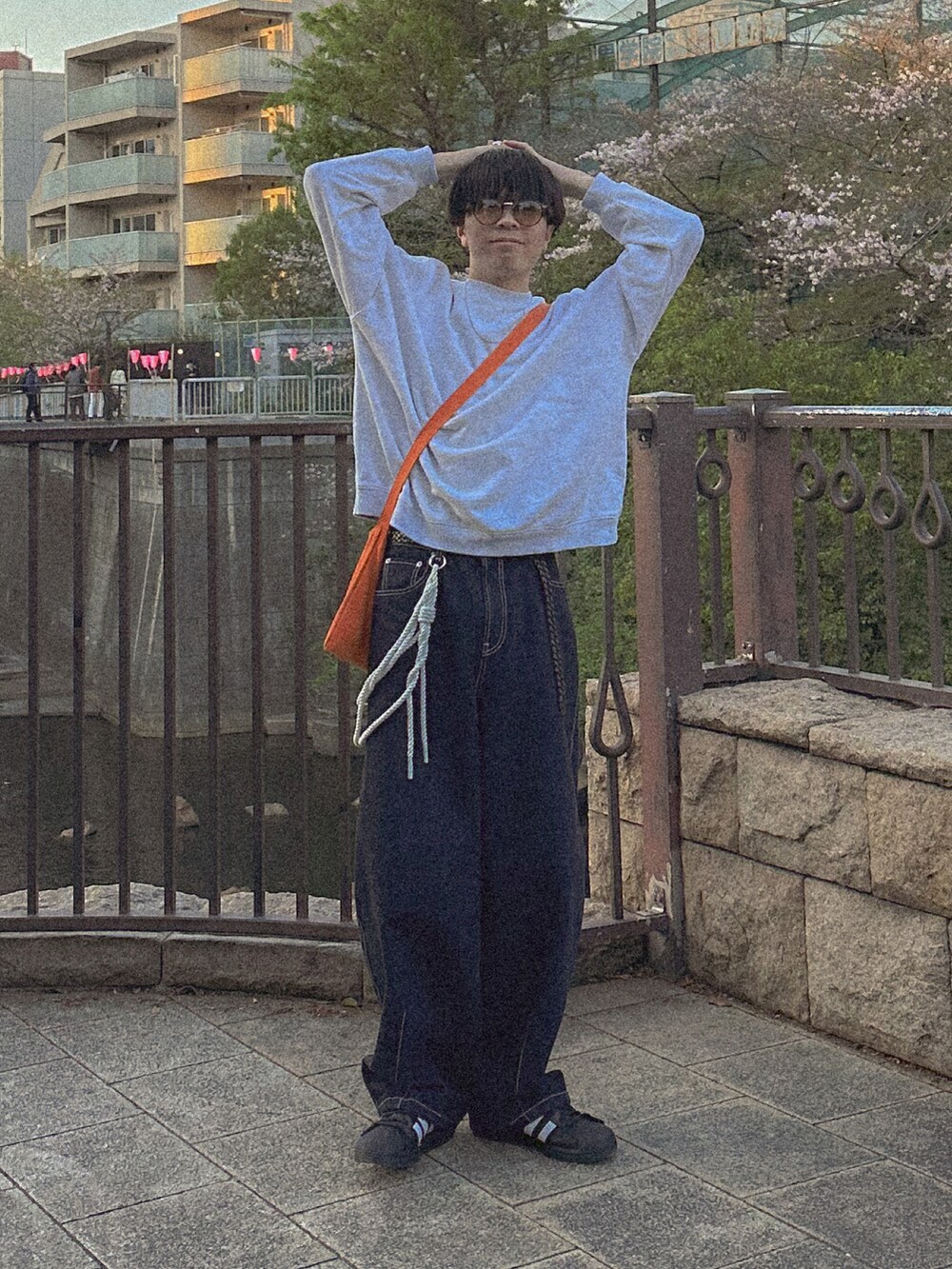 グレー系のスウェット、ブルー系のデニムパンツ、オレンジ系のショルダーバッグを着用したメンズの春コーディネートの2枚目の写真