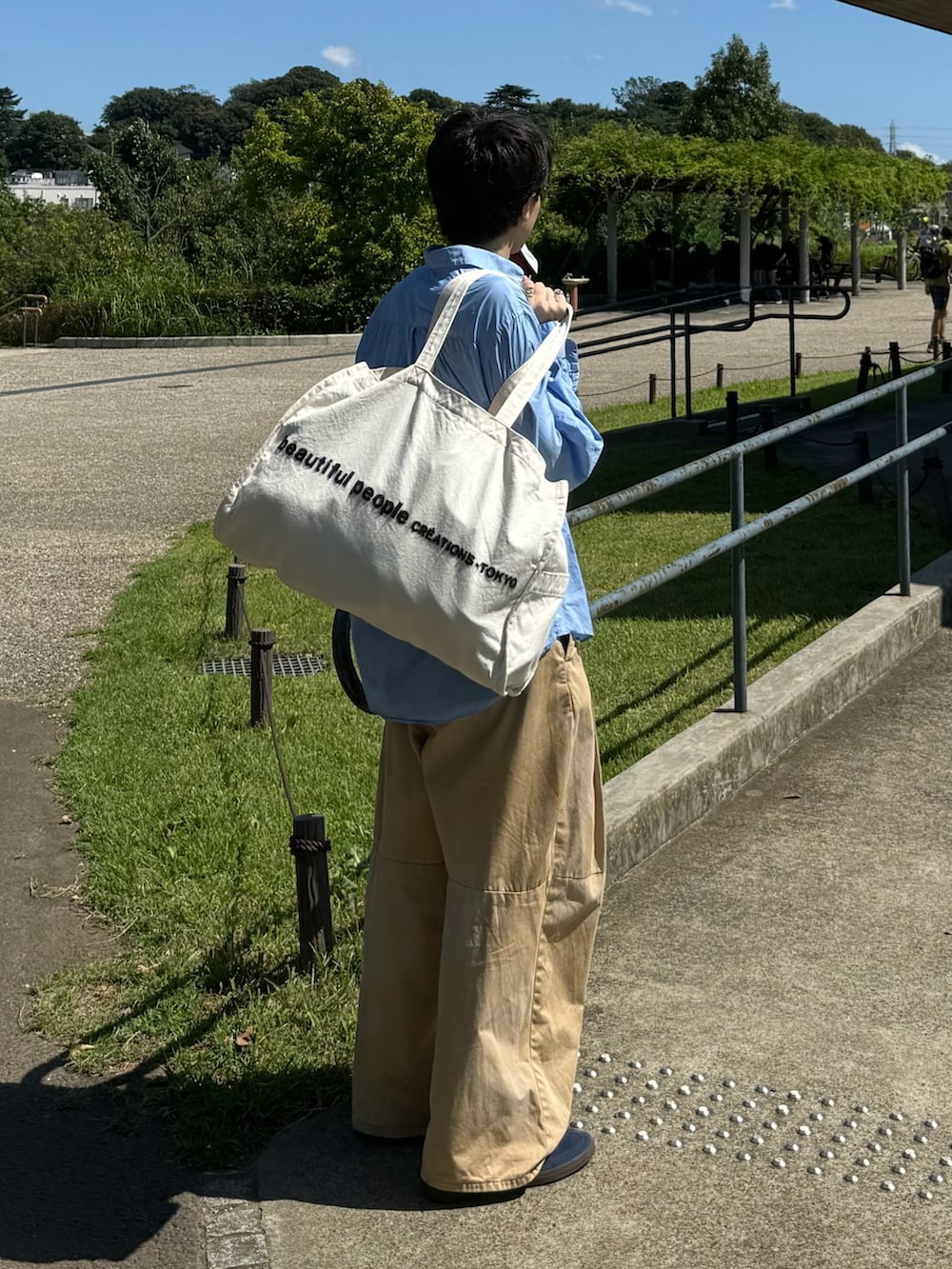 ブルー系のシャツ/ブラウス、ベージュ系のチノパンツ、ベージュ系のトートバッグを着用したメンズの秋コーディネートの2枚目の写真