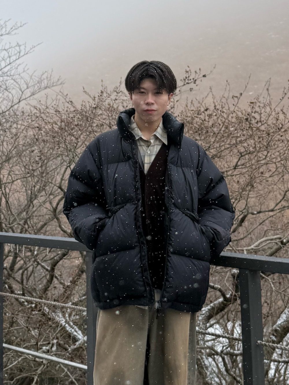 ブラック系のダウンジャケット/コート、ブラウン系のカーディガン/ボレロ、ベージュ系のシャツ/ブラウスを着用したメンズの冬コーディネートの2枚目の写真