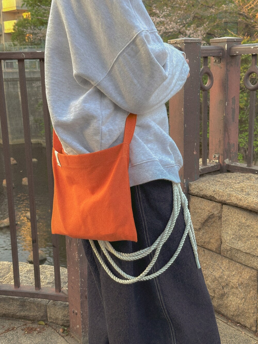 グレー系のスウェット、ブルー系のデニムパンツ、オレンジ系のショルダーバッグを着用したメンズの春コーディネートの4枚目の写真