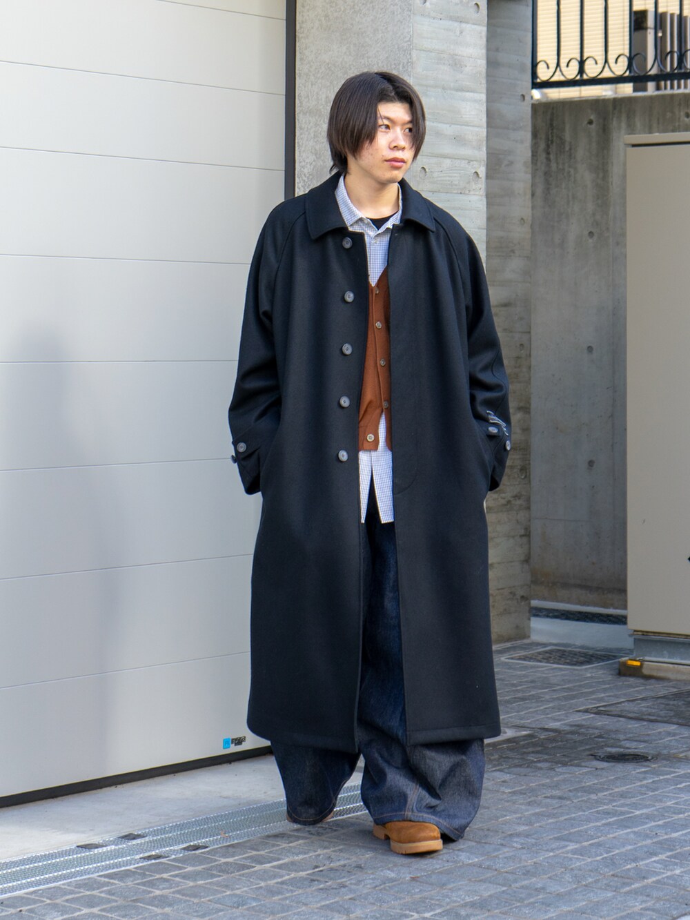 ブラック系のステンカラーコート、ブラウン系のカーディガン/ボレロ、ブルー系のデニムパンツを着用したメンズの冬コーディネートの2枚目の写真
