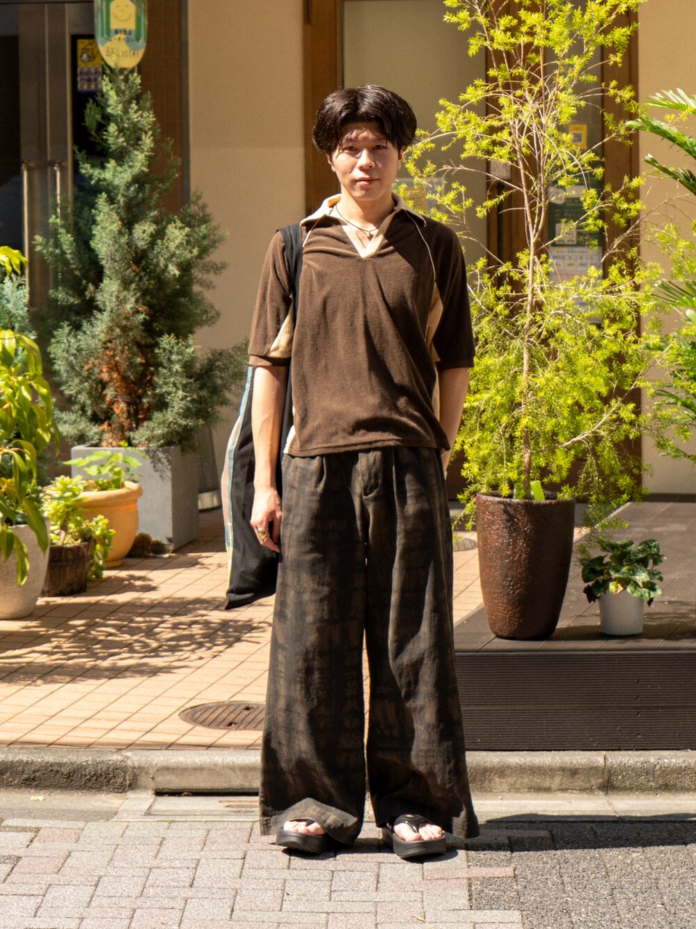 ブラウン系のポロシャツ、グリーン系のその他パンツ、ブラック系のトートバッグを着用したメンズの夏コーディネートの2枚目の写真