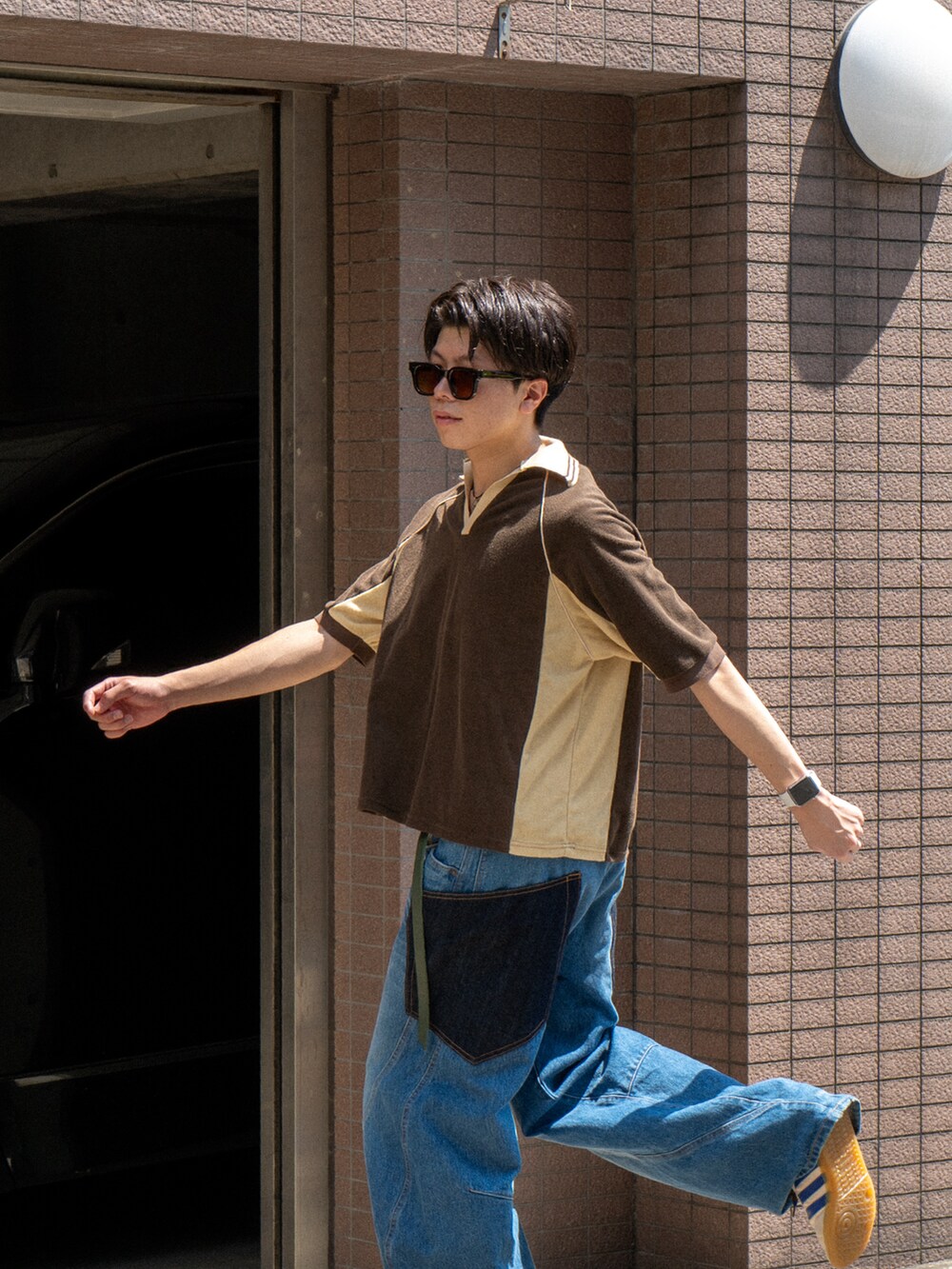 ブラウン系のポロシャツ、ブルー系のデニムパンツ、ホワイト系のスニーカーを着用したメンズの夏コーディネートの4枚目の写真