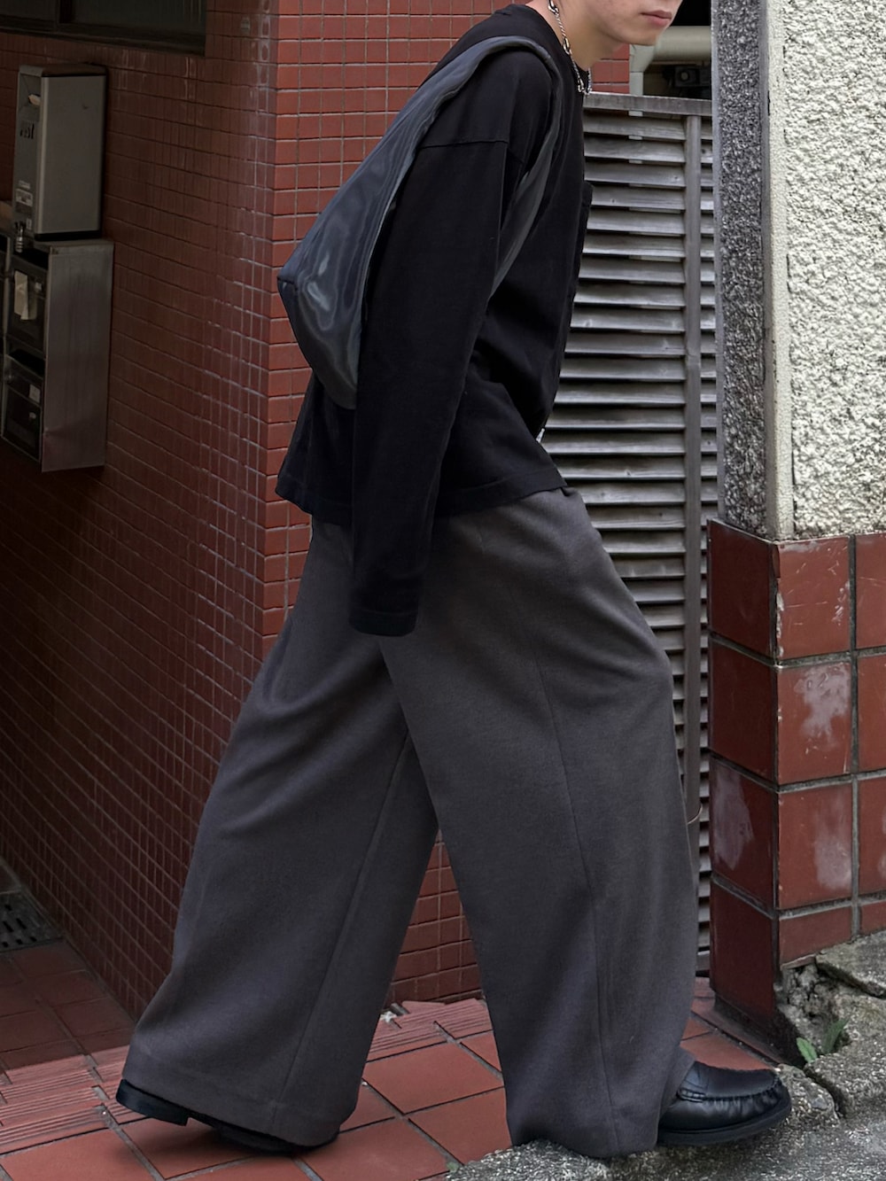 ブラック系のTシャツ/カットソー、ブラウン系のスラックス、グレー系のハンドバッグを着用したメンズの秋コーディネートの4枚目の写真