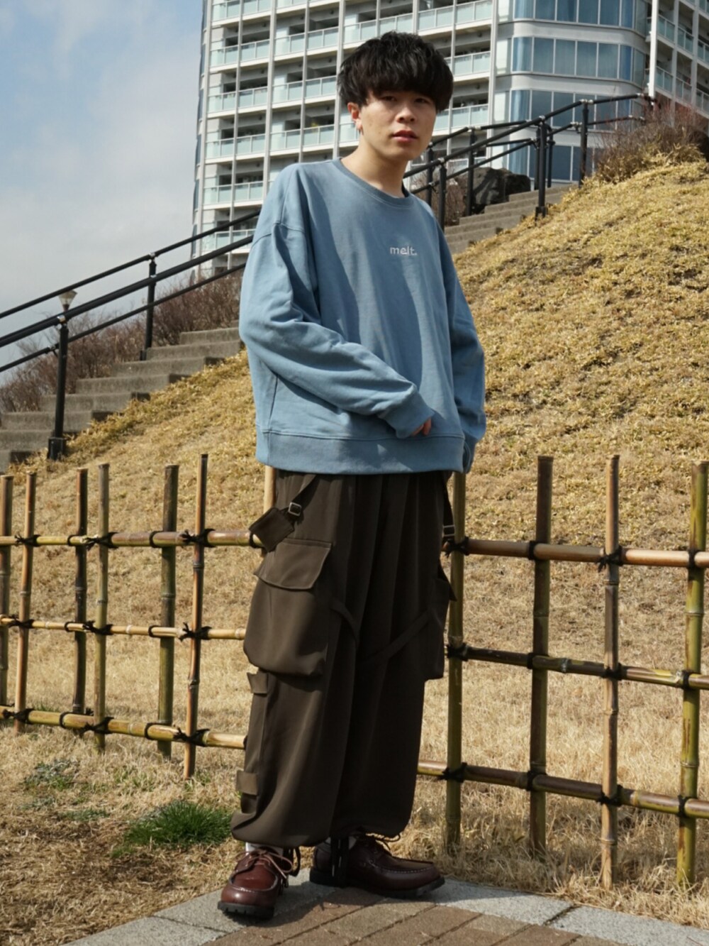 ブルー系のスウェット、グリーン系のサロペット/オーバーオール、ブラウン系のモカシン/デッキシューズを着用したメンズの冬コーディネートの2枚目の写真