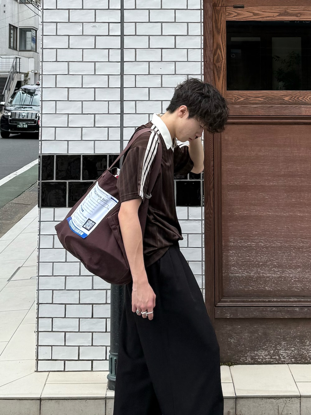 ブラウン系のTシャツ/カットソー、ブラック系のスラックス、ブラウン系のトートバッグを着用したメンズの夏コーディネートの4枚目の写真