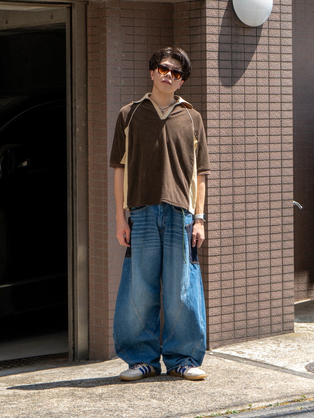 ブラウン系のポロシャツ、ブルー系のデニムパンツ、ホワイト系のスニーカーを着用したメンズの夏コーディネートの2枚目の写真