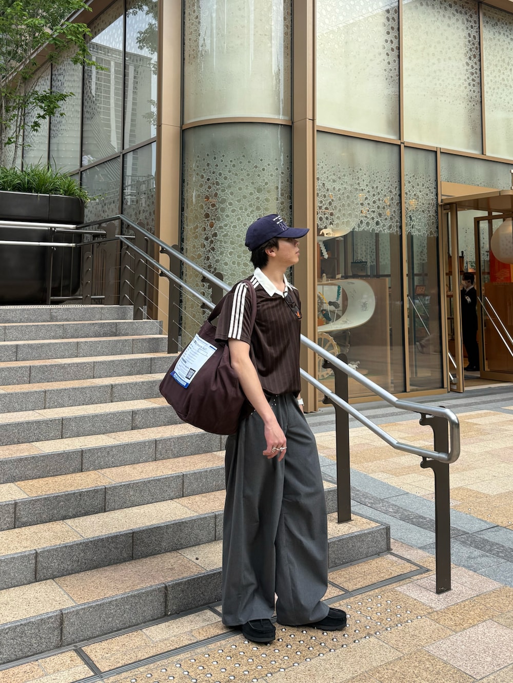 ブラウン系のTシャツ/カットソー、グレー系のスラックス、ブラウン系のトートバッグを着用したメンズの夏コーディネートの3枚目の写真