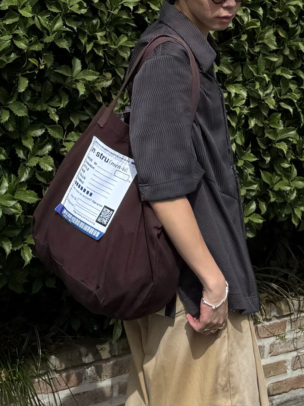 ベージュ系のチノパンツ、ブラウン系のトートバッグ、グレー系のトップスを着用したメンズの夏コーディネートの3枚目の写真