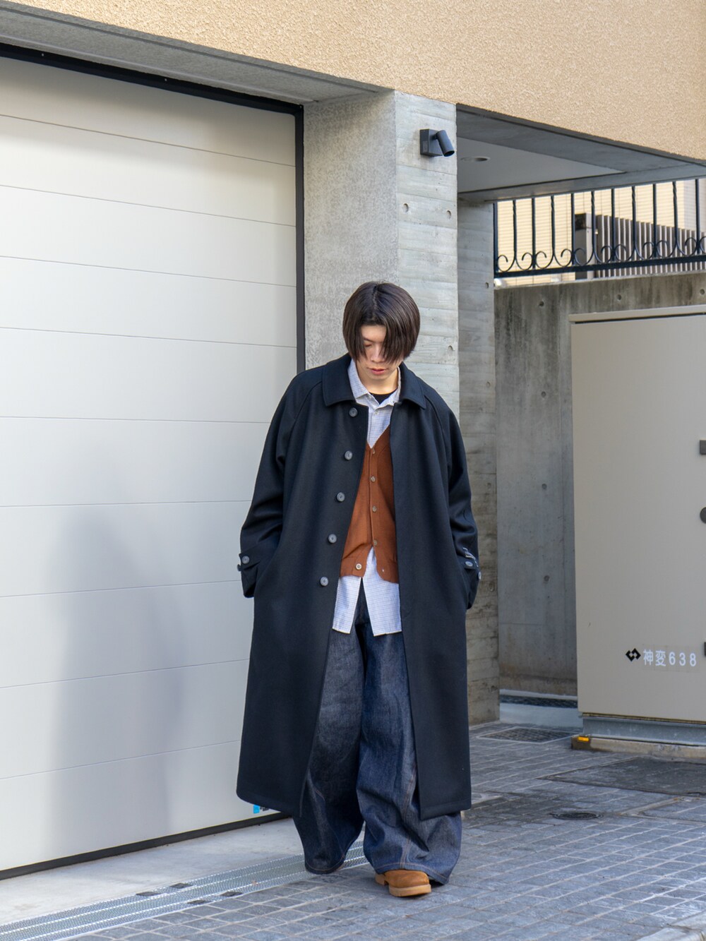 ブラック系のステンカラーコート、ブラウン系のカーディガン/ボレロ、ブルー系のデニムパンツを着用したメンズの冬コーディネートの3枚目の写真