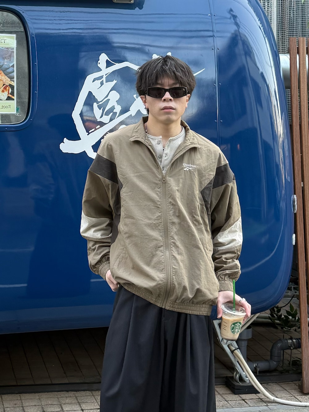 ベージュ系のナイロンジャケット、ベージュ系のTシャツ/カットソー、グレー系のスラックスを着用したメンズの春コーディネートの2枚目の写真