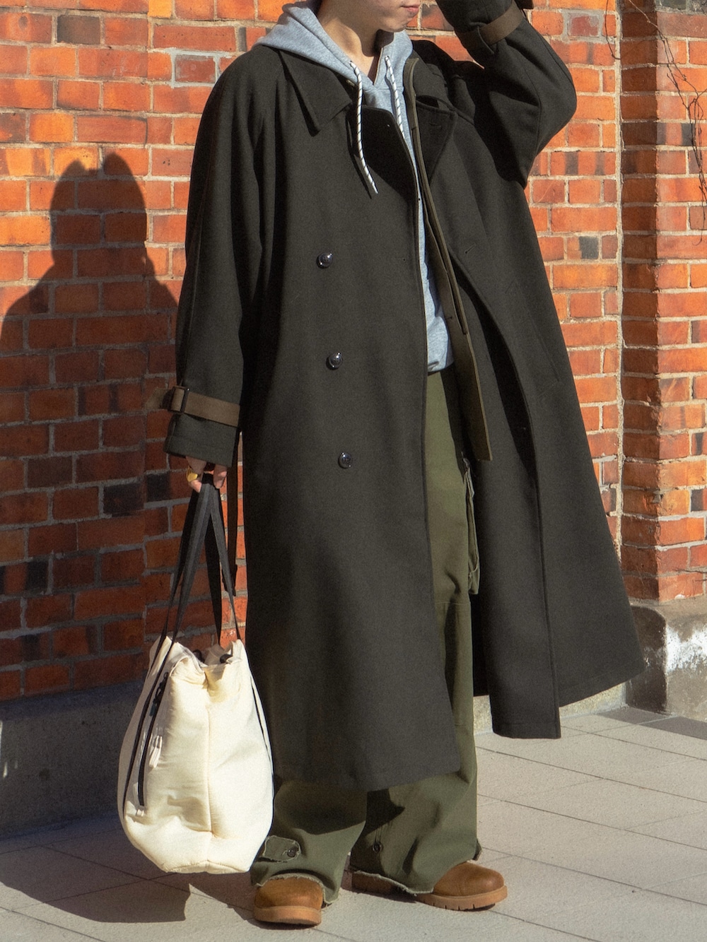 グリーン系のステンカラーコート、グレー系のパーカー、ブラック系のカバーオールを着用したメンズの春コーディネートの5枚目の写真