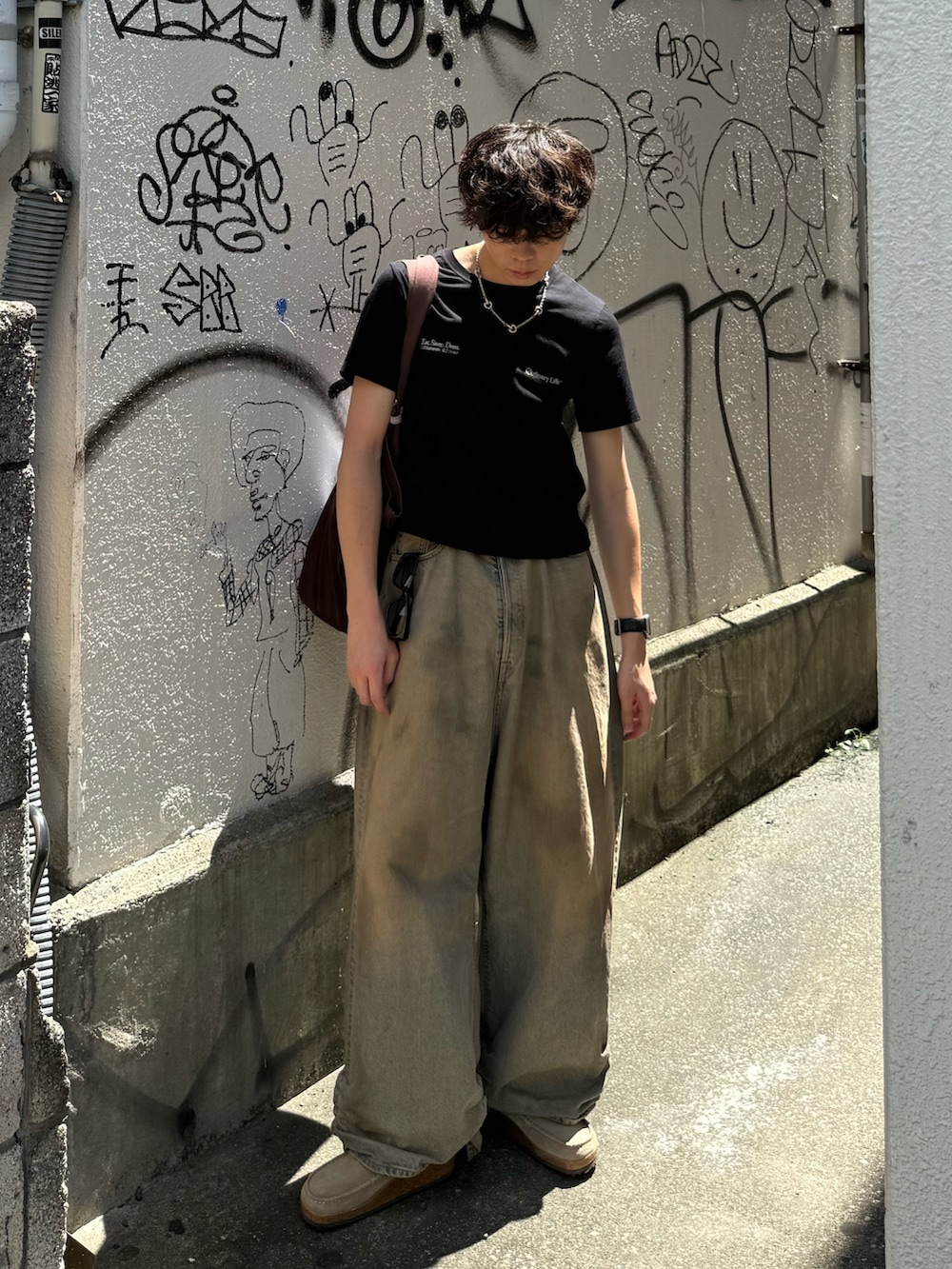 ブラック系のTシャツ/カットソー、ブルー系のデニムパンツ、ブラウン系のトートバッグを着用したメンズの夏コーディネートの2枚目の写真