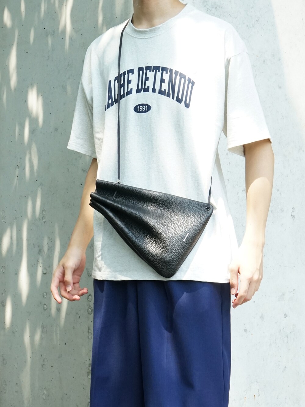 グレー系のTシャツ/カットソー、ブルー系のスラックス、ブラック系のショルダーバッグを着用したメンズの夏コーディネートの5枚目の写真