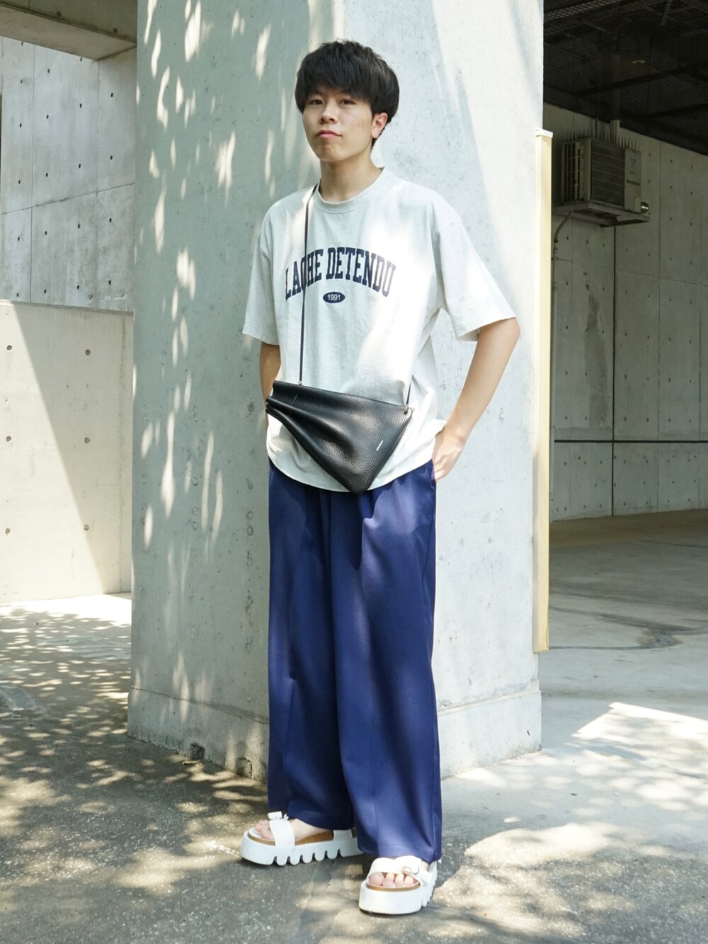 グレー系のTシャツ/カットソー、ブルー系のスラックス、ブラック系のショルダーバッグを着用したメンズの夏コーディネートの3枚目の写真