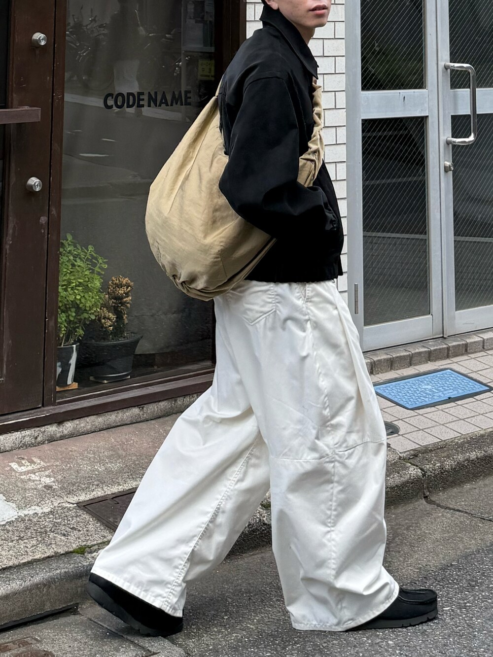 ブラック系のブルゾン、ホワイト系のその他パンツ、ベージュ系のショルダーバッグを着用したメンズの秋コーディネートの2枚目の写真