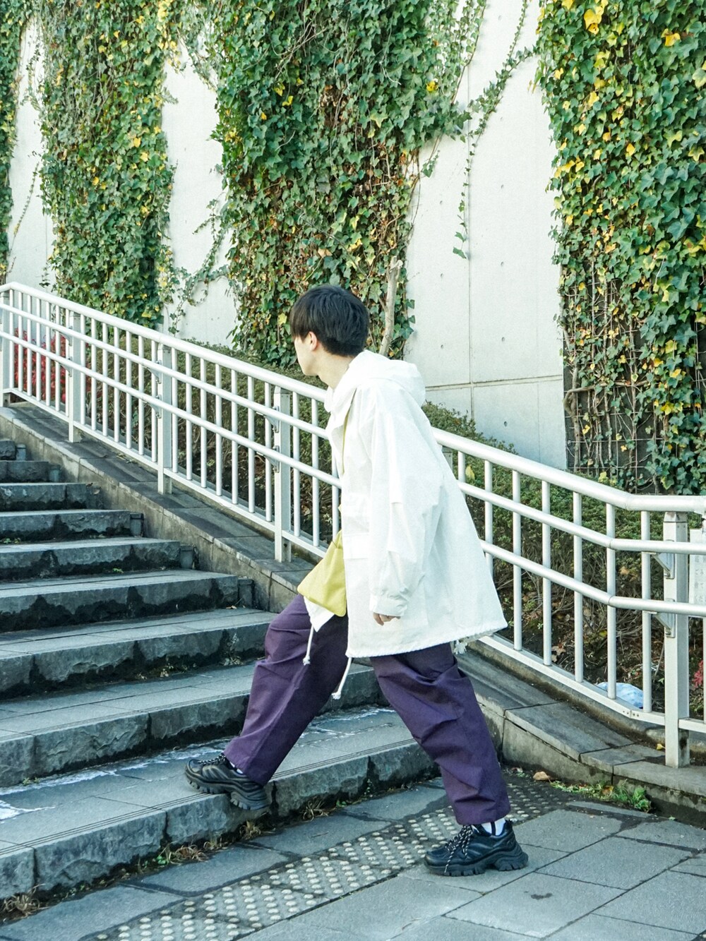 ホワイト系のマウンテンパーカー、イエロー系のショルダーバッグ、ブラック系のスニーカーを着用したメンズの春コーディネートの3枚目の写真