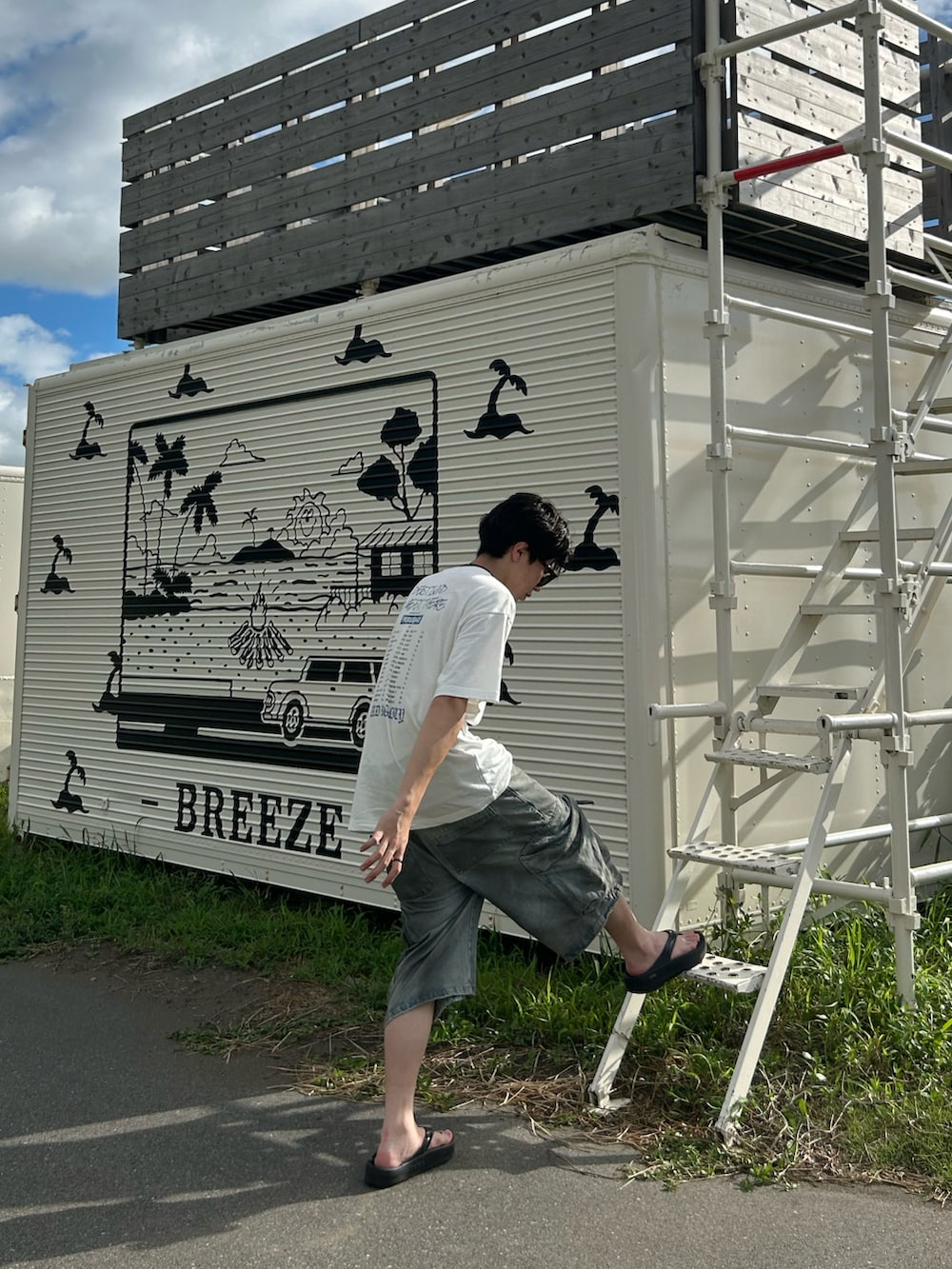 ホワイト系のTシャツ/カットソー、ブルー系のデニムパンツ、ブラック系のサンダルを着用したメンズの夏コーディネートの3枚目の写真