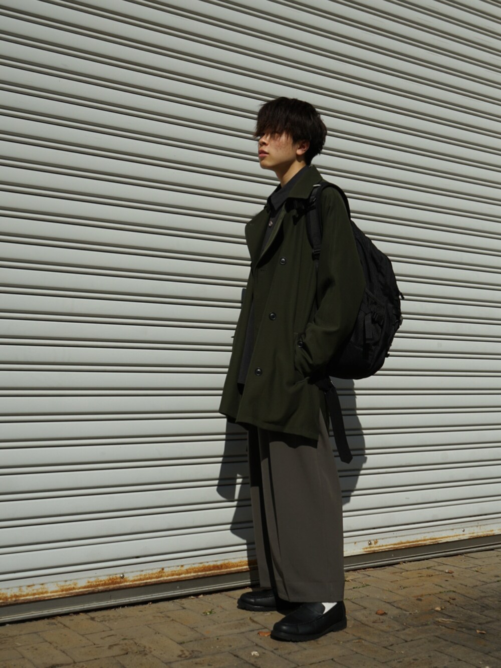 グリーン系のピーコート、ブラック系のバックパック/リュック、グレー系のシャツ/ブラウスを着用したメンズの冬コーディネートの2枚目の写真