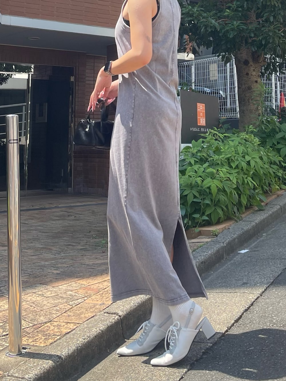 グレー系のワンピース、ブラック系のハンドバッグ、ホワイト系のパンプスを着用したレディースの夏コーディネートの2枚目の写真