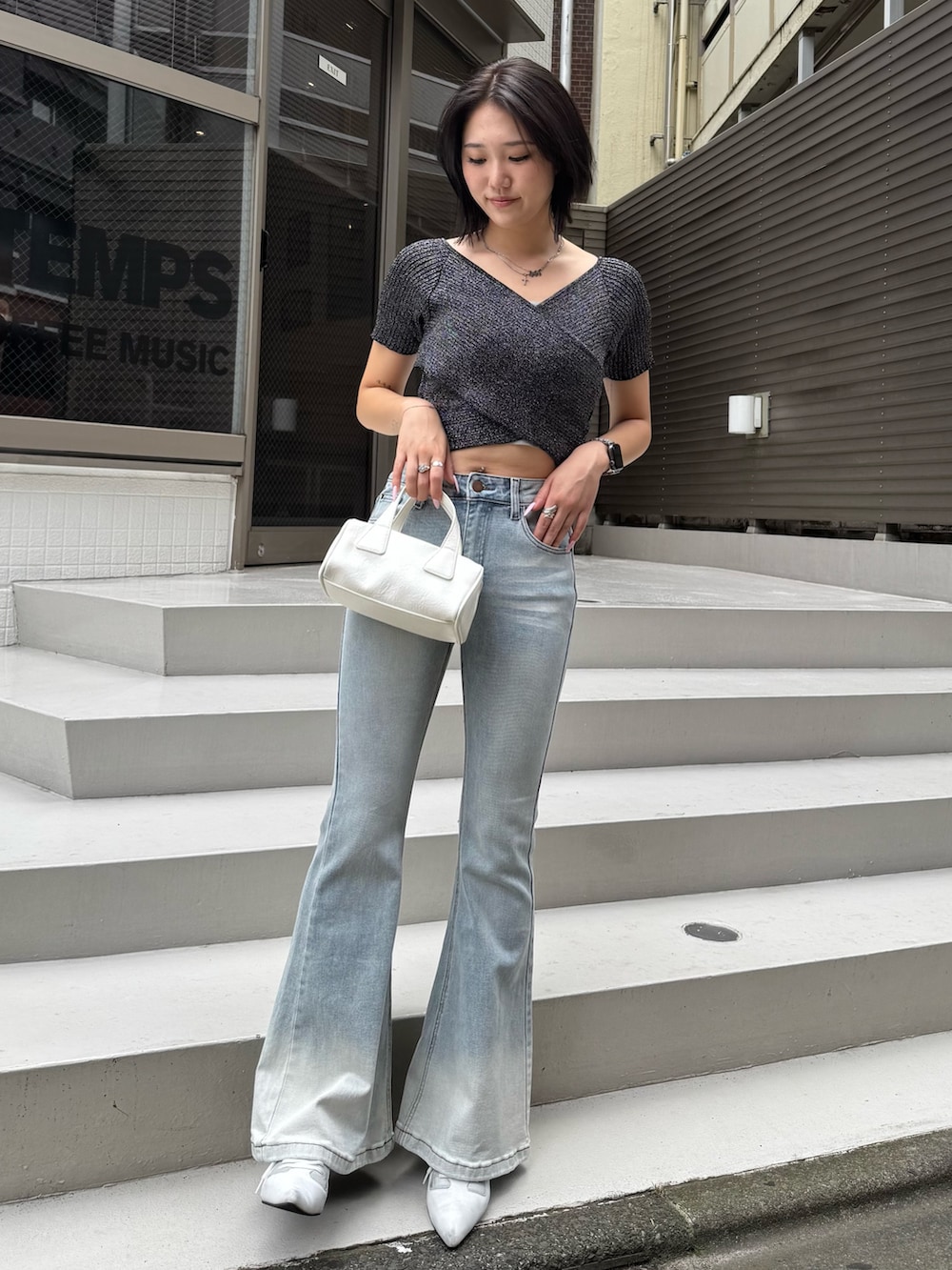 ブラック系のニット/セーター、ブルー系のデニムパンツ、ホワイト系のハンドバッグを着用したレディースの夏コーディネートの2枚目の写真