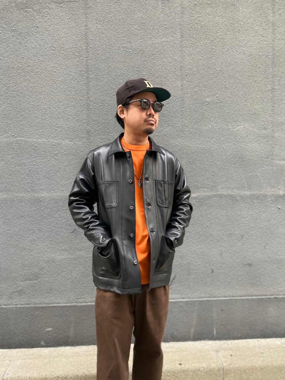 ブラウン系のチノパンツ、ブラック系のライダースジャケット、オレンジ系のTシャツ/カットソーを着用したメンズの冬コーディネートの2枚目の写真