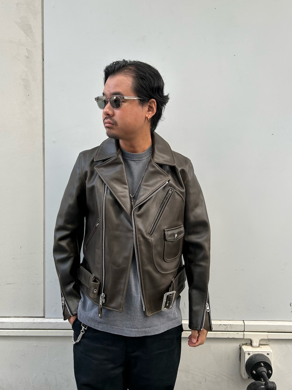 グリーン系のライダースジャケット、ブラック系のチノパンツ、ブラック系のブーツを着用したメンズの秋コーディネートの2枚目の写真