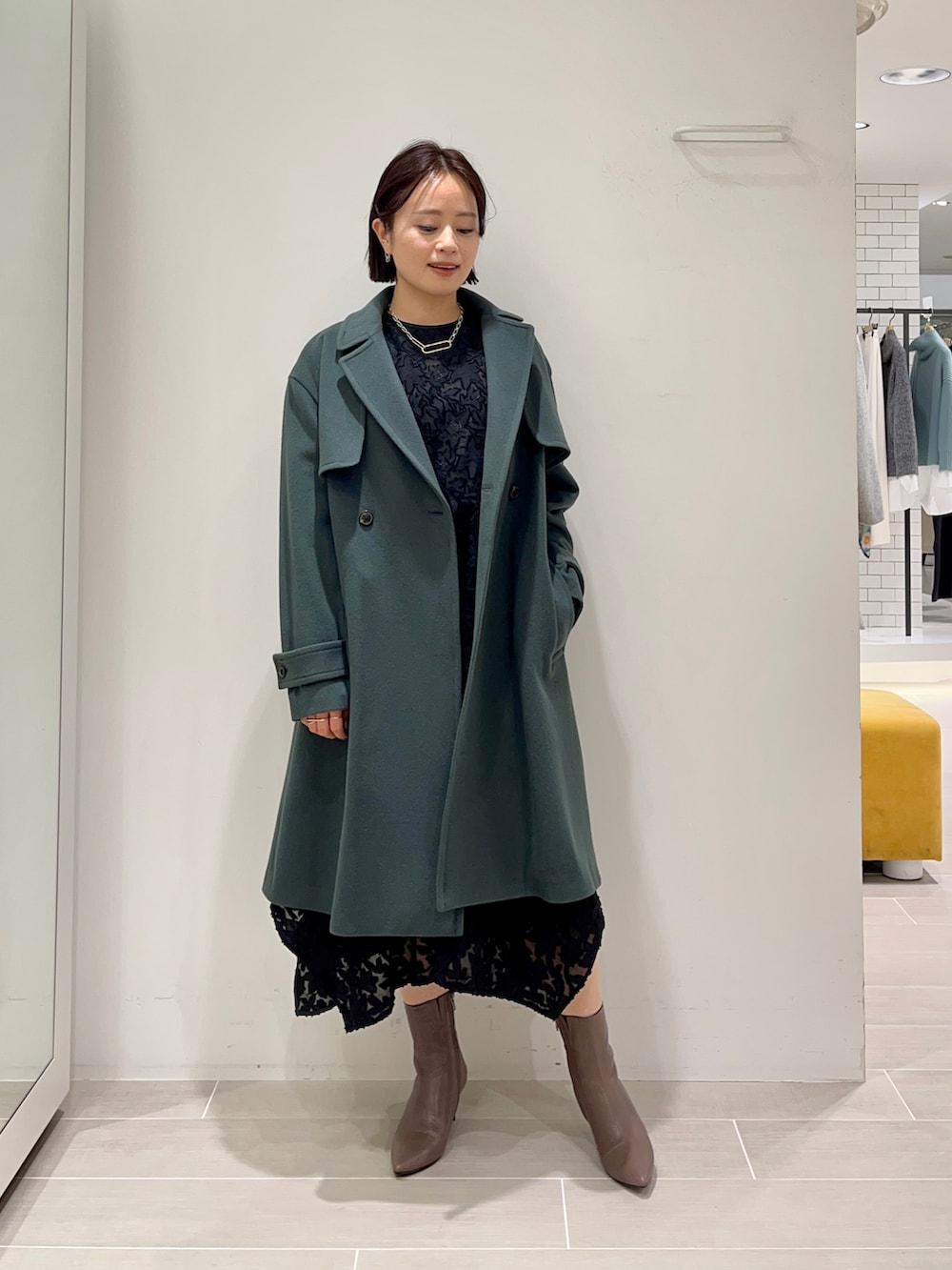 グリーン系のトレンチコート、ブラック系のワンピースを着用したレディースの冬コーディネートの2枚目の写真