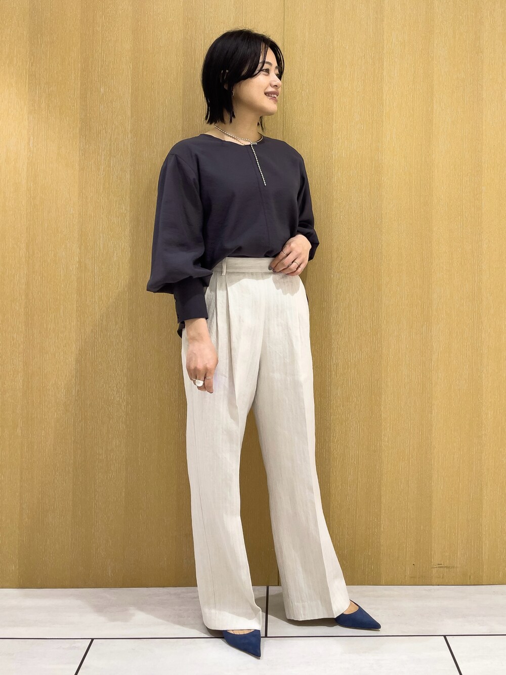 ベージュ系のスラックス、グレー系のシャツ/ブラウス、シルバー系のネックレスを着用したレディースの春コーディネートの2枚目の写真