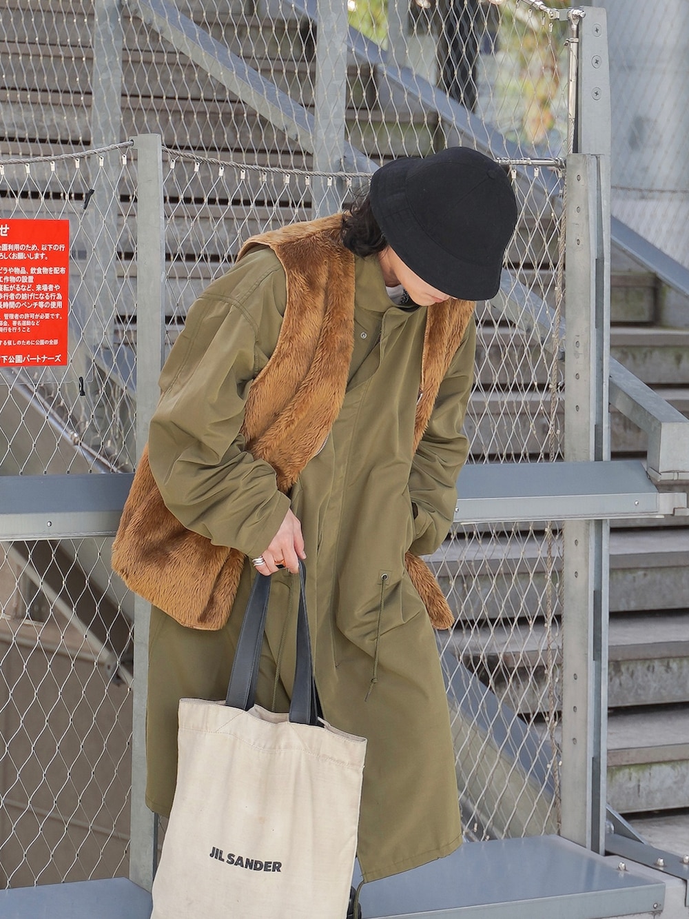 グリーン系のモッズコート、ブラウン系のベスト、ベージュ系のトートバッグを着用したメンズの秋コーディネートの2枚目の写真