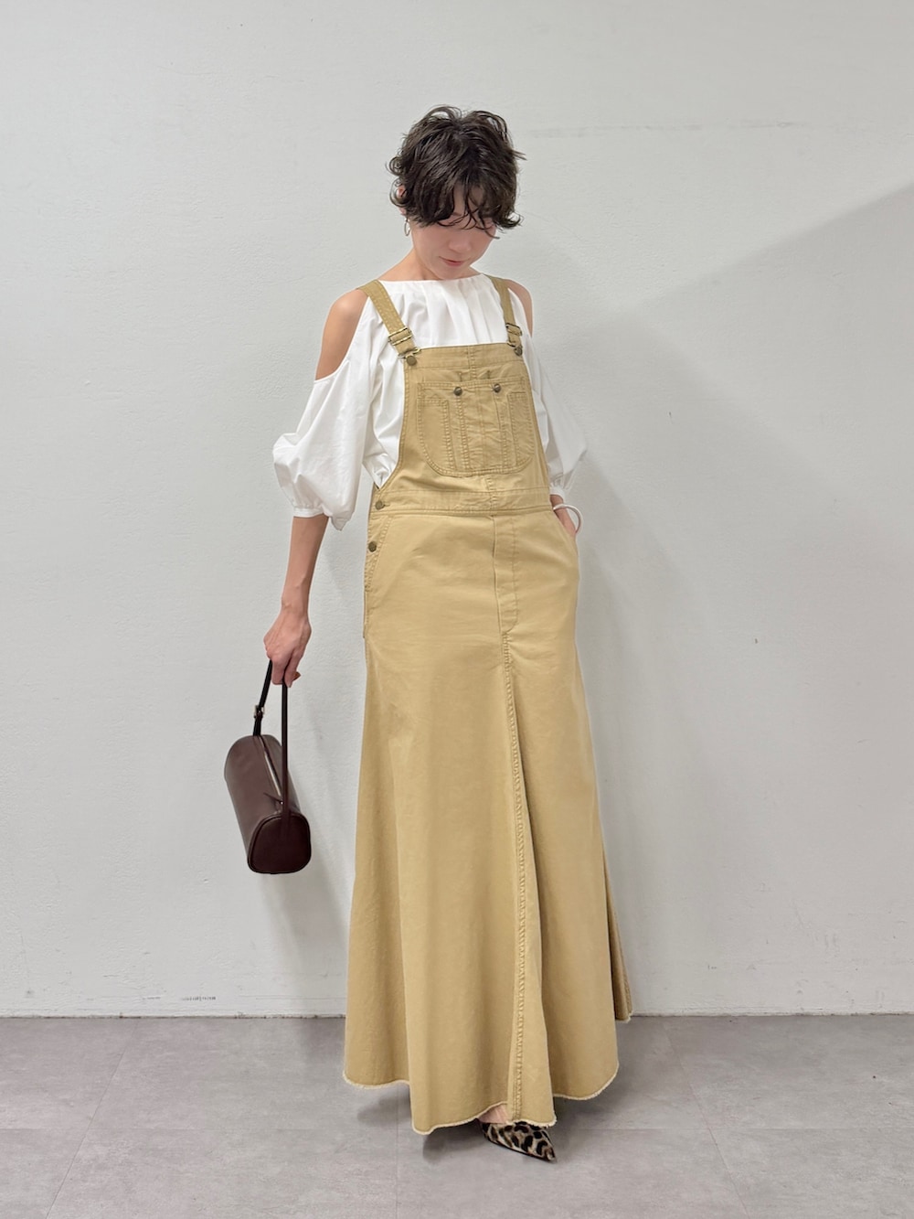 イエロー系のジャンパースカート、ブラウン系のショルダーバッグ、イエロー系のパンプスを着用したレディースの冬コーディネートの2枚目の写真