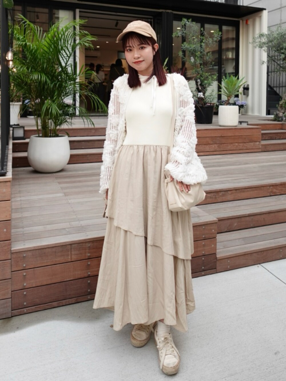 ベージュ系のワンピース、ホワイト系のカーディガン/ボレロ、ホワイト系のスニーカーを着用したレディースの春コーディネートの2枚目の写真