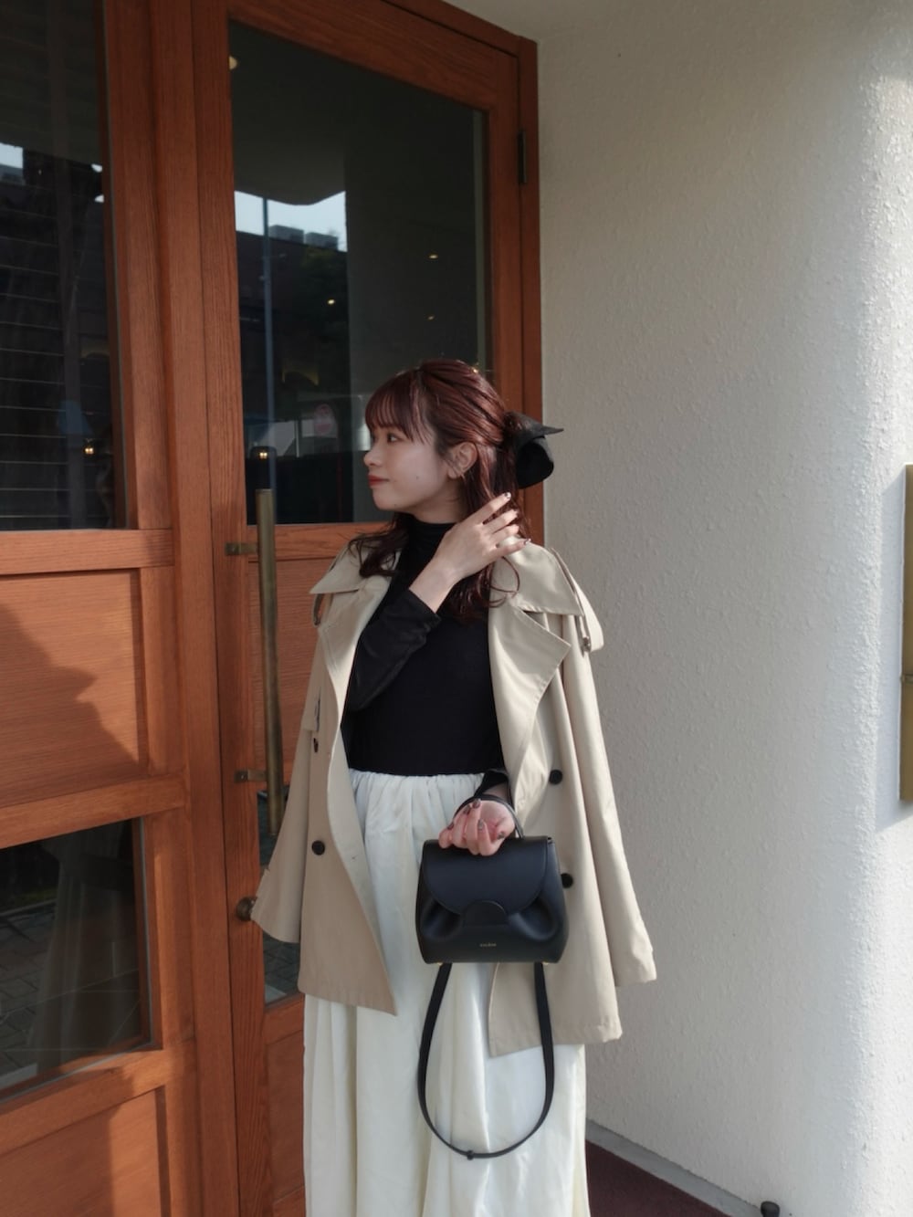 ベージュ系のトレンチコート、ホワイト系のスカート、ブラック系のニット/セーターを着用したレディースの冬コーディネートの3枚目の写真
