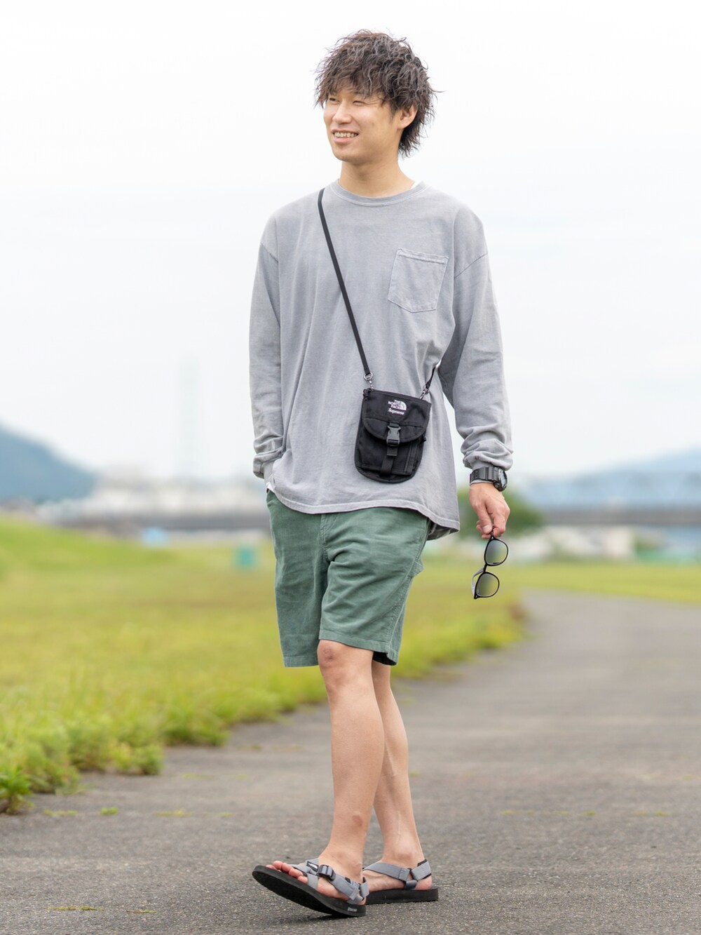 グレー系のTシャツ/カットソー、ブラック系のショルダーバッグ、グリーン系のパンツを着用したメンズの夏コーディネートの2枚目の写真