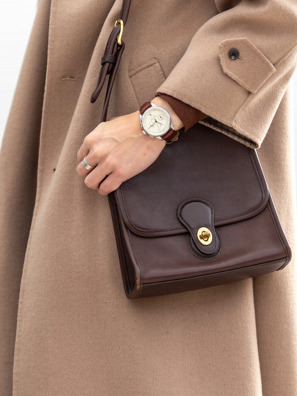 ベージュ系のステンカラーコート、ホワイト系のTシャツ/カットソー、ブラウン系のニット/セーターを着用したメンズの冬コーディネートの2枚目の写真