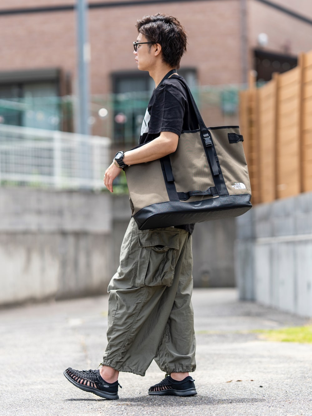 ブラック系のTシャツ/カットソー、グリーン系のトートバッグ、グリーン系のカーゴパンツを着用したメンズの夏コーディネートの2枚目の写真