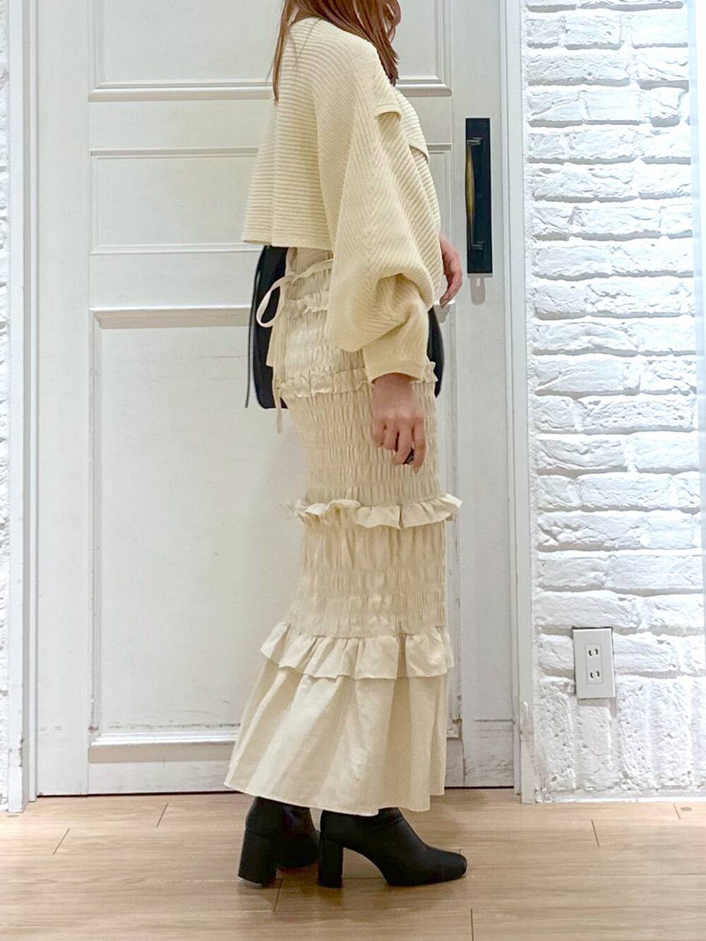 ホワイト系のニット/セーター、ブラック系のブーツ、ブラック系のショルダーバッグを着用したレディースの秋コーディネートの4枚目の写真